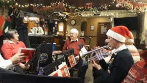 BAnd members wearing Christmas jumpers and hats play carols in a pub