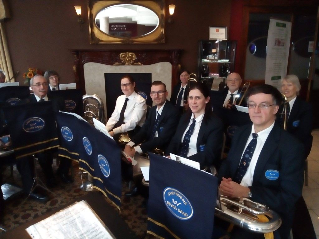 Band members wearing their uniforms are sat with their instruments on their laps