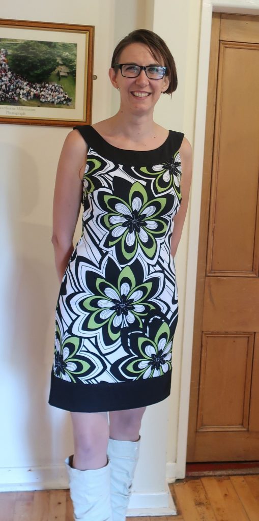 Jen is wearing a short green black and white dress with high white boots.