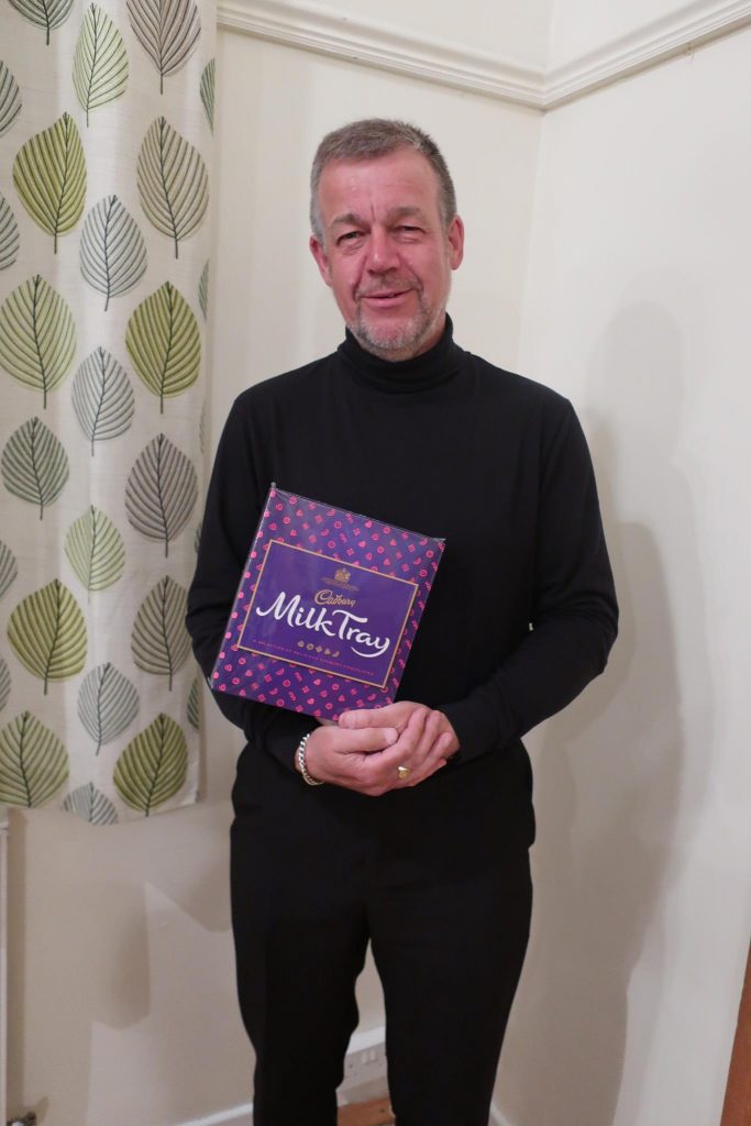 Martin is wearing all black and holding a box of milk tray