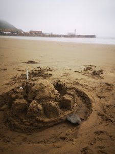 a sandcastle is in the foreground. There is a lighthouse in the mist in the background